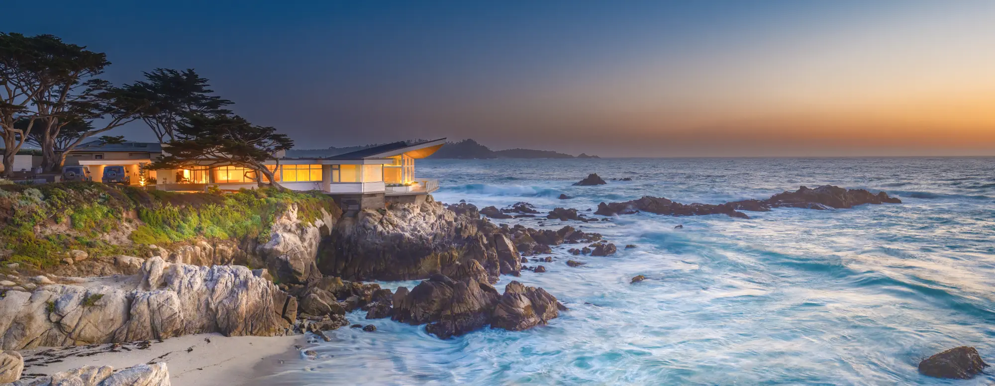 Oceanfront home glowing at dusk above the rocks at Carmel Point, Carmel-by-the-Sea